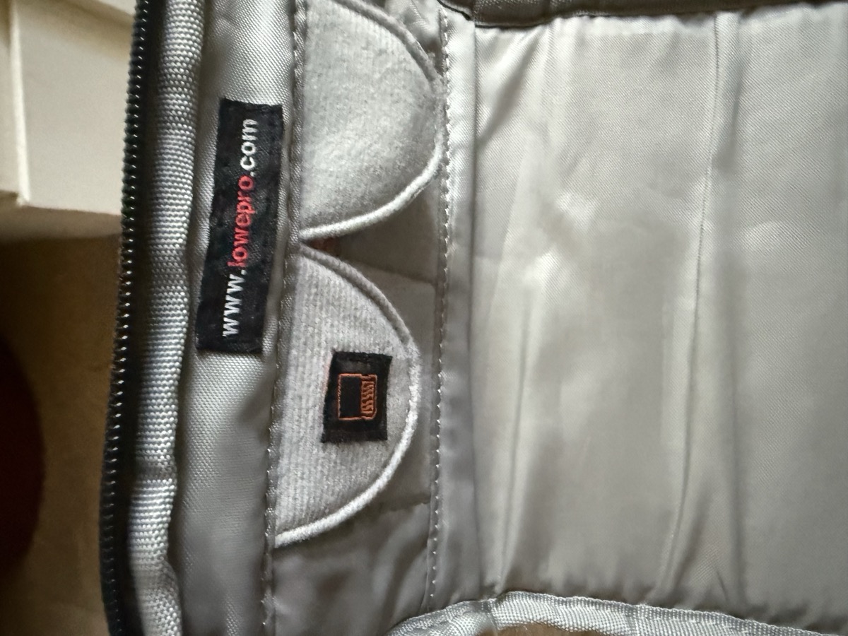 Close-up of the Lowepro Slingshot 202 AW interior brand tags showing the www.lowepro.com woven label alongside the tan SlipLock modular-attachment tag on the silver-gray padded lining