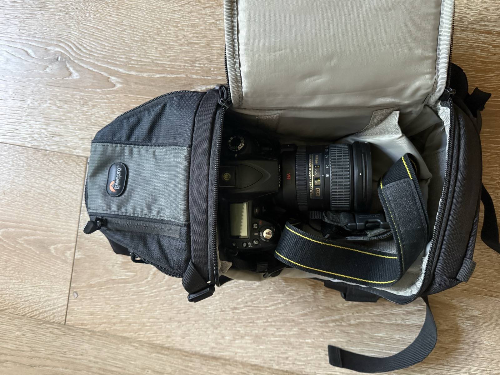 Interior of the Lowepro Slingshot 202 AW with the side flap open, holding a Nikon full-frame DSLR with a 24-70mm f/2.8 lens attached, sitting on the silver ProtectiveGripper padded lining