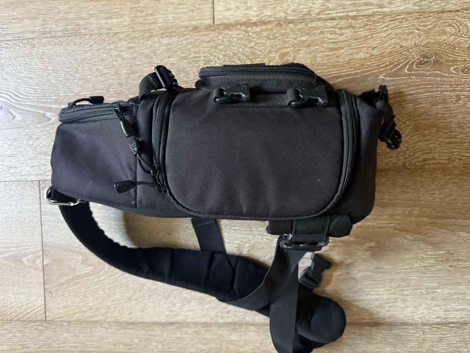 Side profile of the Lowepro Slingshot 202 AW closed, showing the front accessory pocket, top grab handle, side compression strap, and the single sling shoulder strap running diagonally